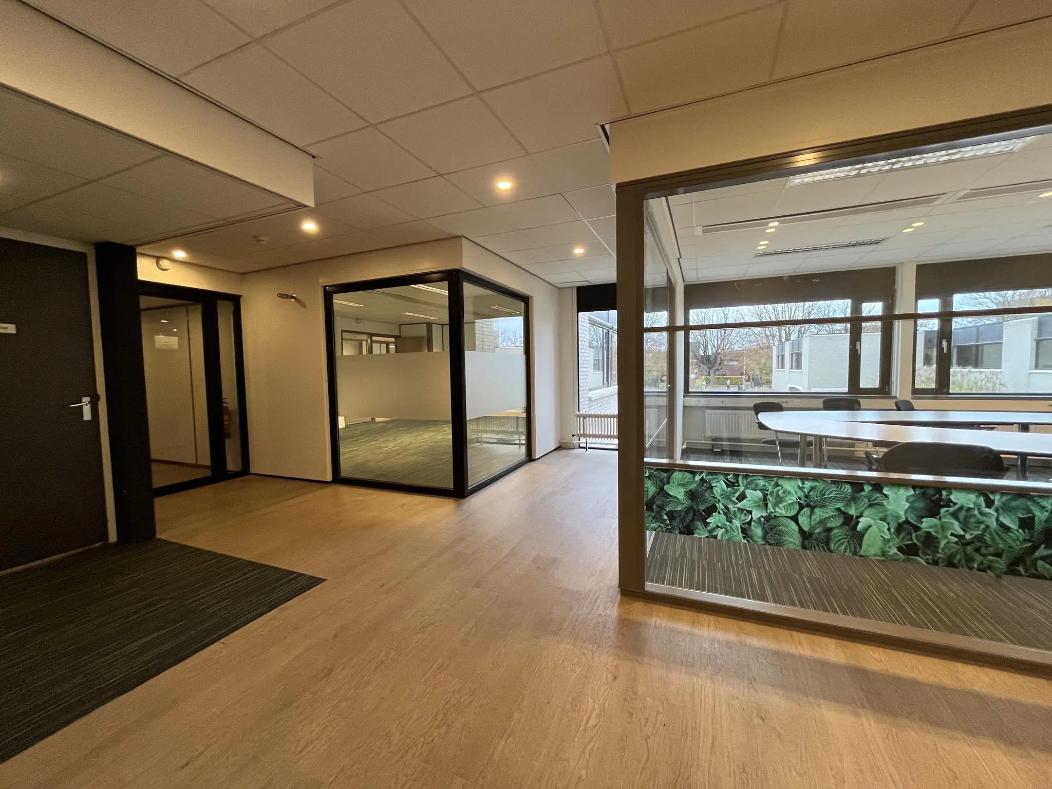 Moderne kantoorruimte aan de Burgemeester Verderlaan met glazen vergaderruimtes en houten vloer.